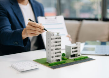 Commercial Property Insurance concept with a man with a pen pointing to model business buildings on desk.