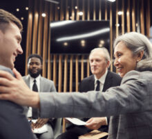 Professional Liability as a group of diverse business people sitting at a table with Asian woman congratulating a young man.