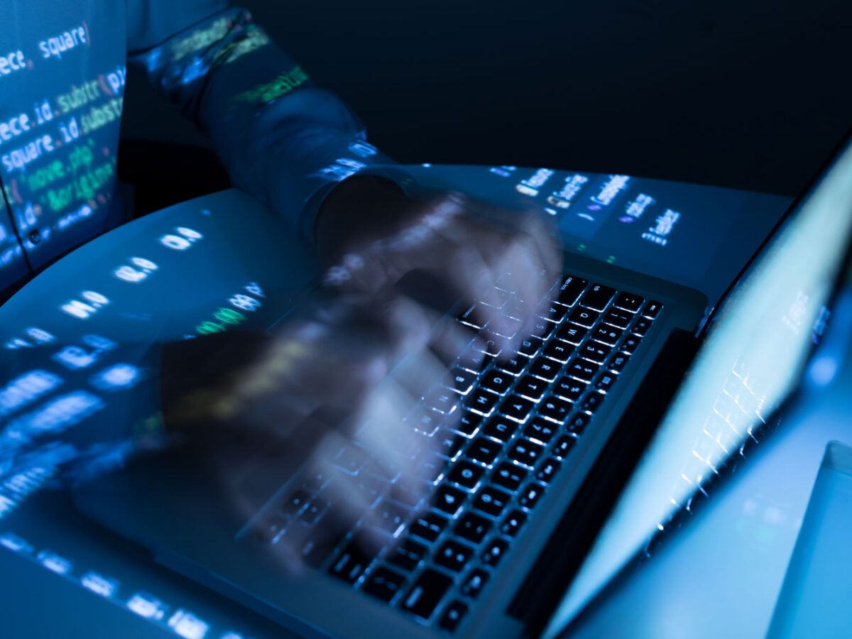 Man's hand typing on a laptop in the dark.