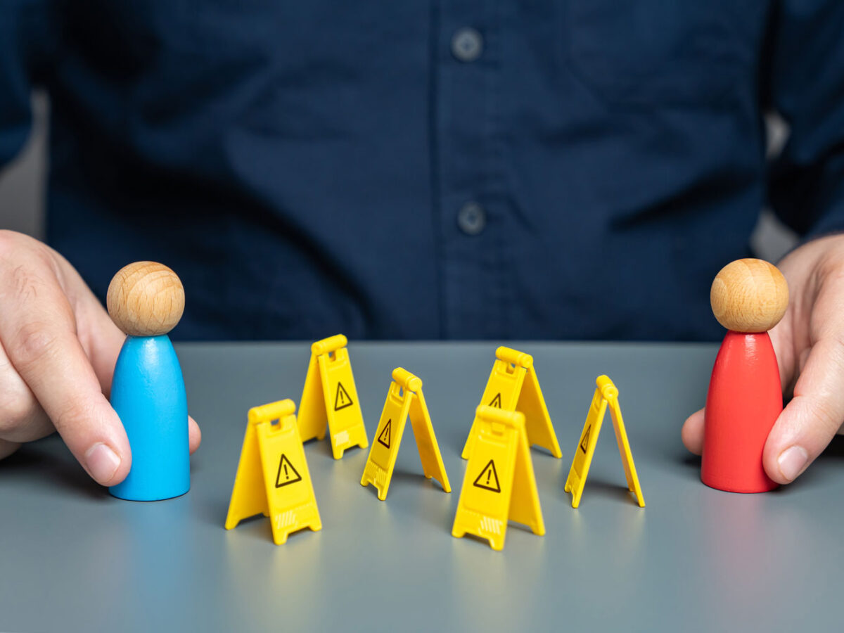 Man hands holding wood people with little yellow caution folding signs between them.
