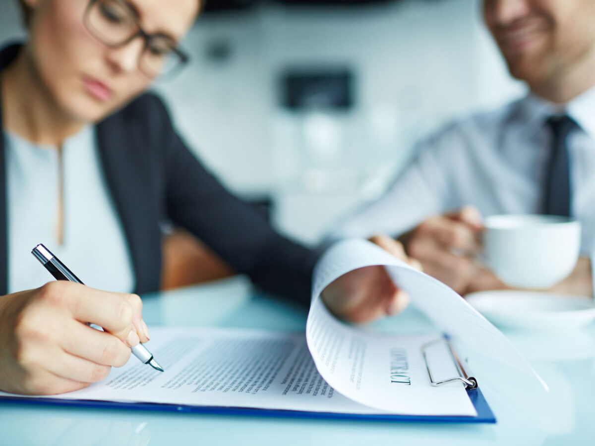 Asian woman signing papers with a business man watching at a table.