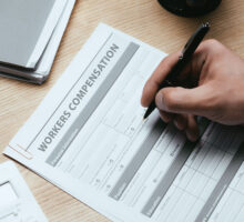 Workers’ Compensation concept with a man's hand filling out worker's compensation papers.