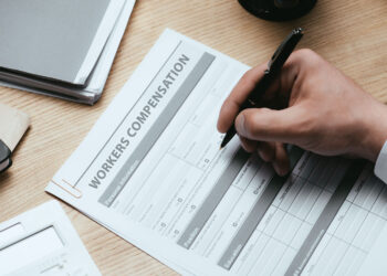 Workers’ Compensation concept with a man's hand filling out worker's compensation papers.